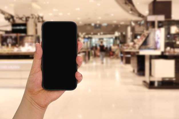 Hand of a man holding smartphone device in the Shopping mall background and have white copy space on screen.