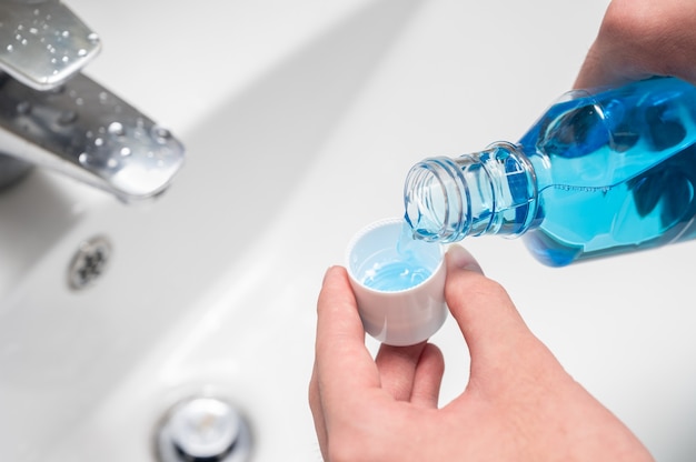 Photo hand of man pouring bottle of mouthwash into cap.