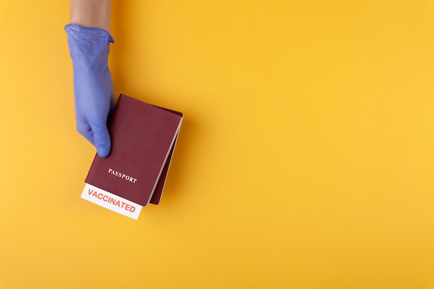 Hand in medical glove holding passport with vaccinated stamp on yellow background