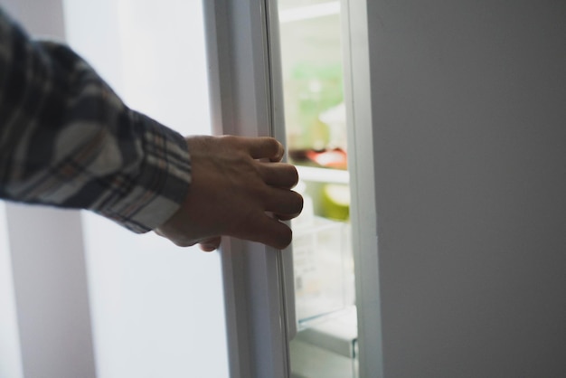 A hand opens fridge in the kitchen to take some food