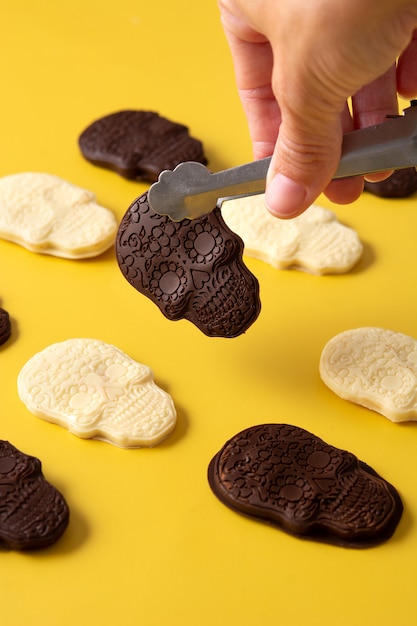 Hand pcking up chocolate Mexican skull with tongs on yellow background