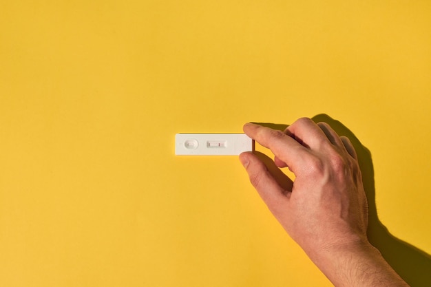 Hand of a person holds a negative coronavirus test on a yellow background