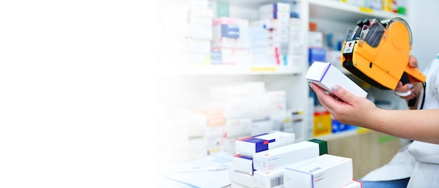 Hand of the pharmacist using yellow labeling gun for sticking price label of medicine in pharmacy