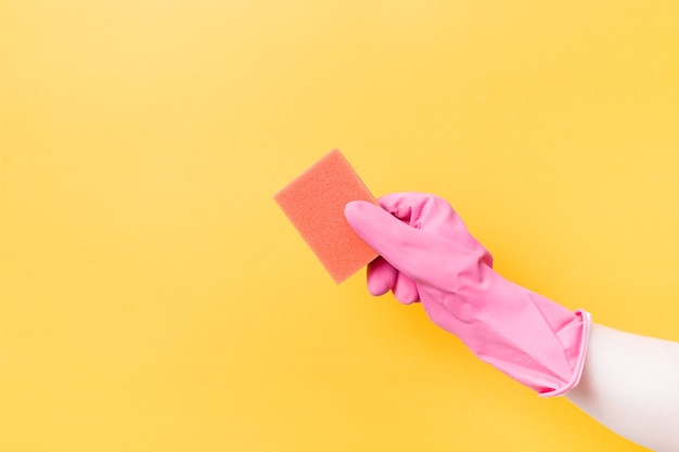 Hand in pink rubber glove holds orange sponge for washing dishes and cleaning