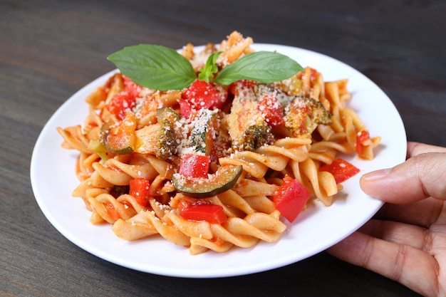 Hand Placing a Plate of Mouthwatering Wholemeal Fusilli Pasta in Tomato Sauce on Wooden table