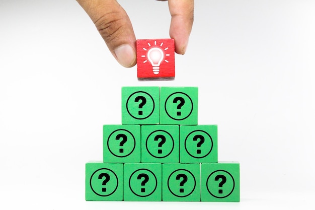 A hand placing a red light bulb on a green cube with a green block that says question.