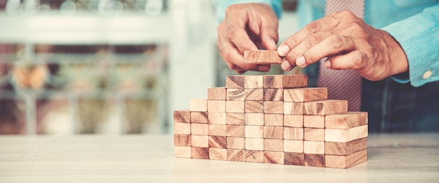 Hand placing wood block tower stack in pyramid stair step