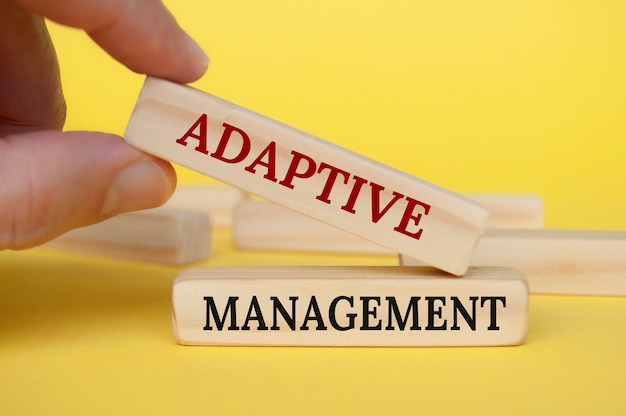 Photo hand placing wooden block on yellow cover with text adaptive management