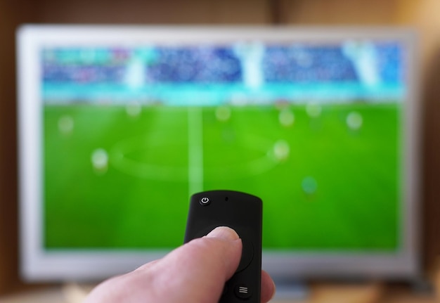 hand pointing remote control at tv set with soccer or football match