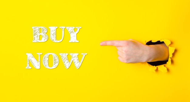 Photo a hand pointing to the word buy now on a yellow background