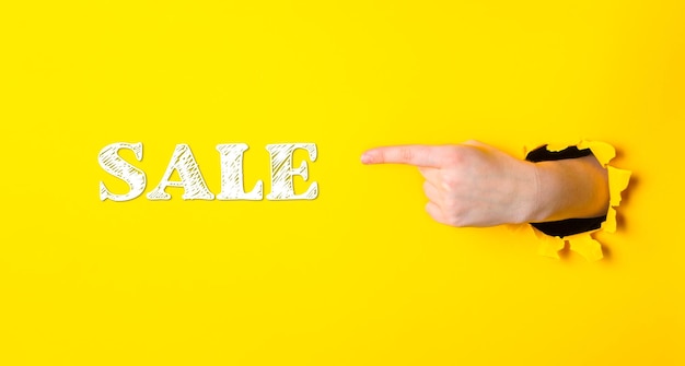 Photo a hand pointing to the word sale on a yellow background