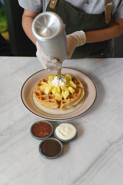 Hand pouring ice cream on Belgium waffles with sliced pineapple