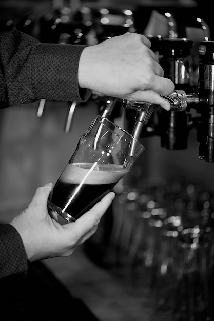 Hand pours a beer in a transparent glass from the tapRetro b W