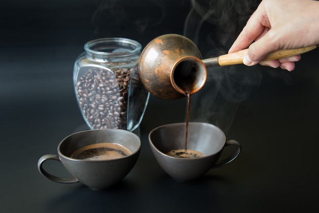 A hand pours black coffee from a vintage Turkish coffee pot