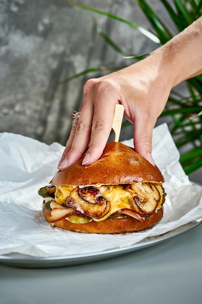 A hand presses a bun burger with mushrooms cheese bacon on white parchment Closeup selective focus