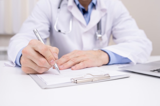 Hand of professional clinician with pen over clipboard with medical document going to make notes or prescription