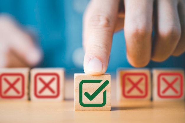 Hand pushing green correct sign symbol in front of Red Cross sign on wooden block cube for business proposal and document approve concept