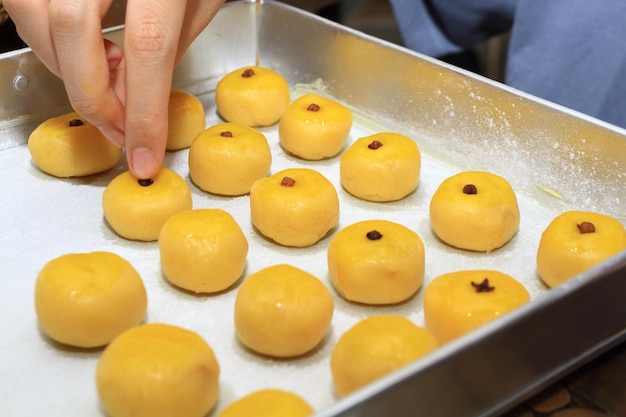 A hand put a clove to each Nastar or Pineapple Tart on aluminum tray before baking