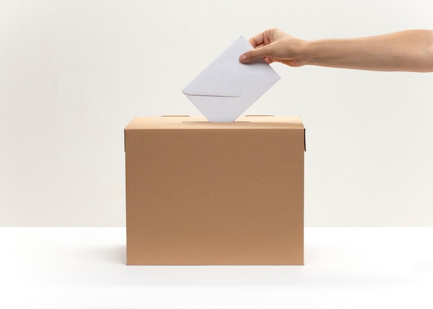 Hand puts white envelope into vote box