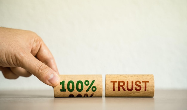 The hand puts wooden blocks with the words 100 percent trust Trust relationships between business partners Respect and authority Confidence in a person Reliability sincerity and competence