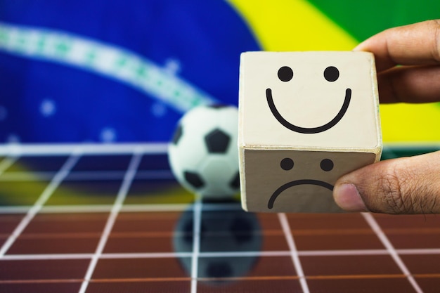 Hand puts wooden cubes with smile face and sad face and Brazil Flag on photovoltaic solar panel Positive Sports Mindset Concept