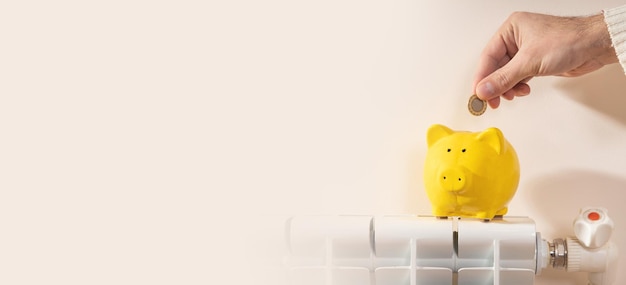 Hand putting coin into piggy bank on heating radiator