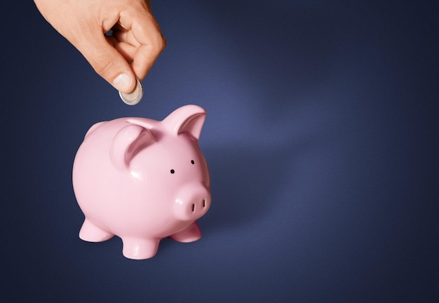 Hand putting coin to piggy bank on blue background