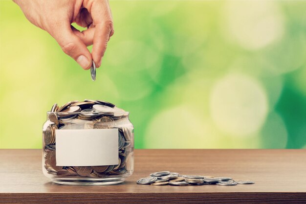 Hand putting Coins in glass jar with blank label for giving and donation concept