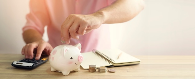 A hand putting money coin into piggy bank. A saving money for future investment concept.