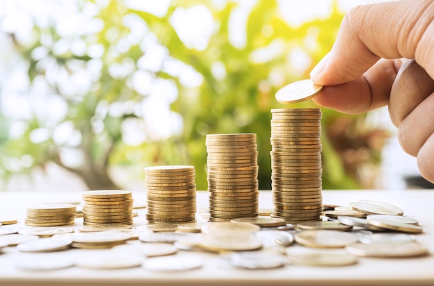 Hand putting money coins stack growing with green and sunlight background.For business growth investment and financial concept ideas.