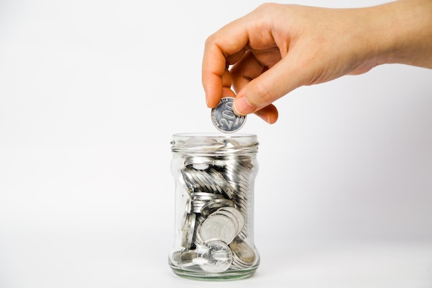 A hand putting one Indonesian silver coin in a glass of jar full shot