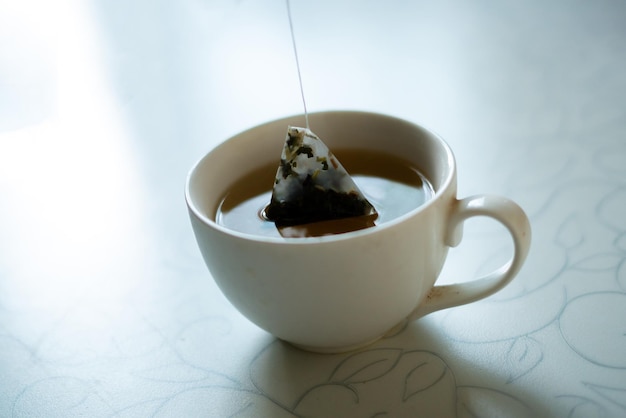 Hand putting a pyramid tea bag in a hot water cup in the morning