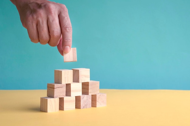 Hand putting a square wood block on pyramid stack of wood blocks