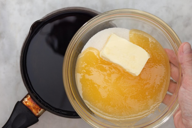 Hand putting sugar butter and honey on saucepan