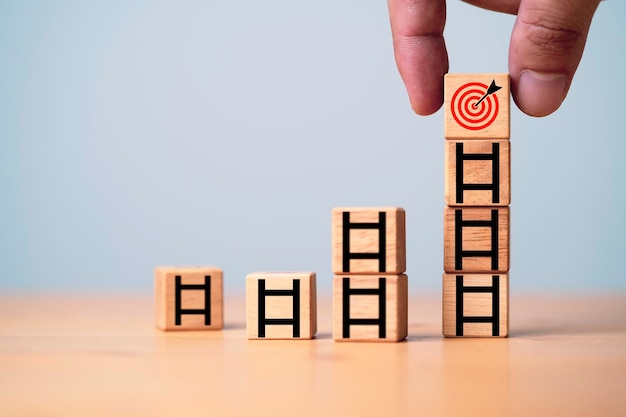 Hand putting target board on the top of ladder which print screen on wooden cube block for growth of business objective and goal concept