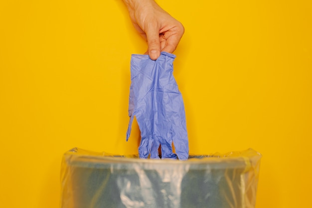 Hand putting used dirty surgical glove to a garbage bin