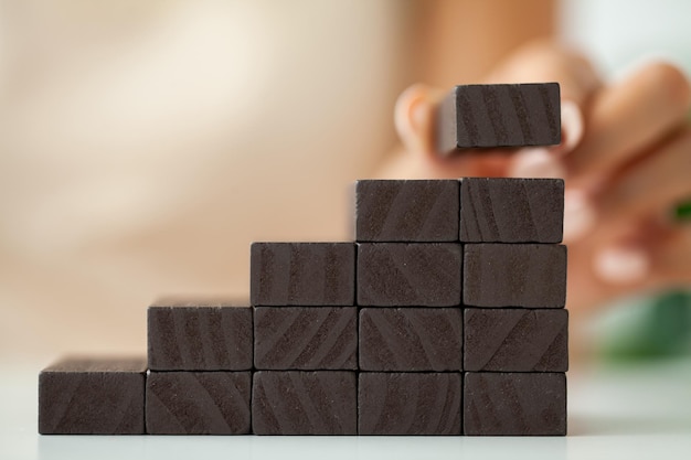 Hand putting wood cube on top of wood block stacking as step stair.