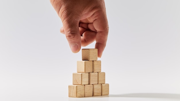 Hand putting wood cubes arranged in the pyramid shape on white