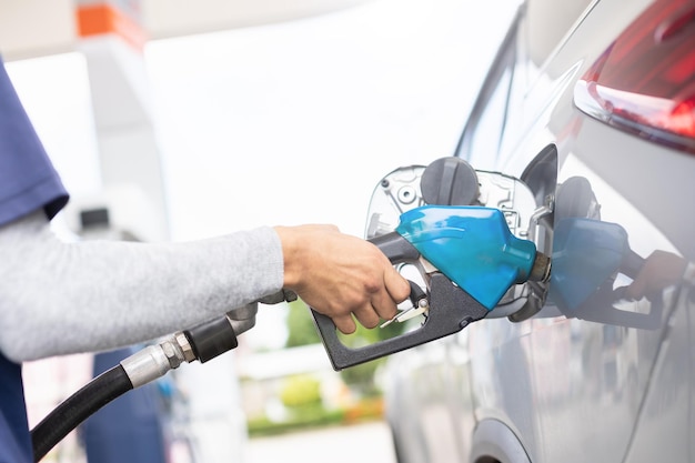 Hand of refueling worker are filling fuel to car in Petrol station Focus on fuel nozzle and blur day light background