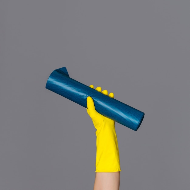 Hand in rubber glove holds blue garbage bag on neutral background. The concept of spring cleaning.