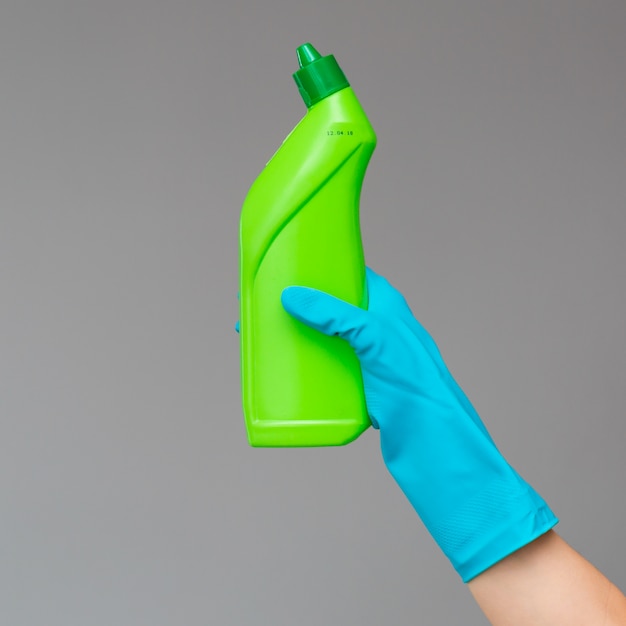 A hand in a rubber glove holds a bottle of plumbing detergent 