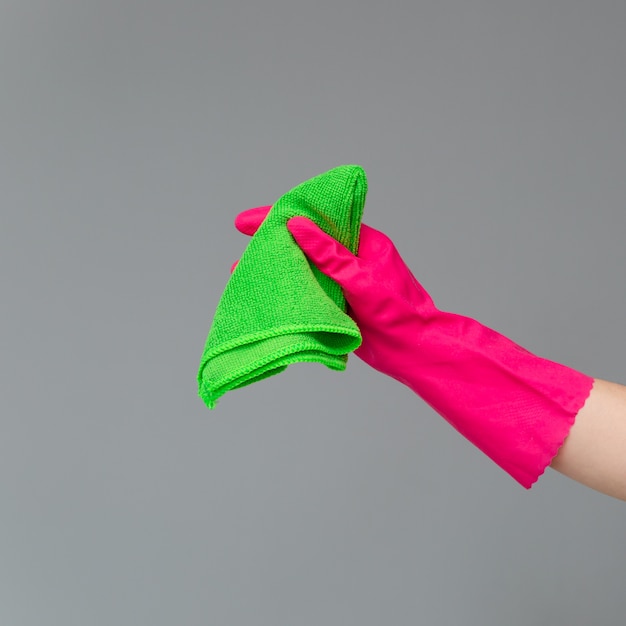 A hand in a rubber glove holds a bright microfiber duster on a neutral background. Ð¡oncept of bright spring, spring cleaning.