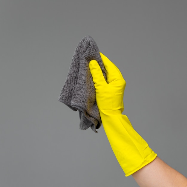 A hand in a rubber glove holds a bright microfiber duster 