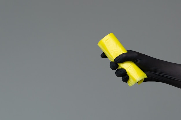 Hand in rubber glove holds colored garbage bag on neutral background