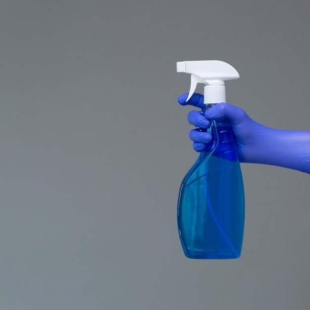 A hand in a rubber glove holds the glass cleaner in a spray bottle on grey