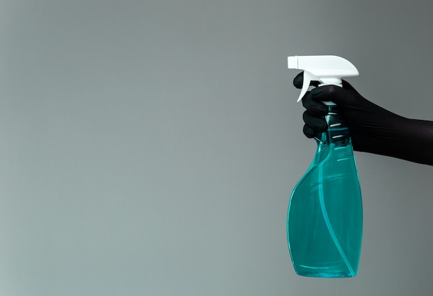 A hand in a rubber glove holds the glass cleaner in a spray bottle on a neutral. 