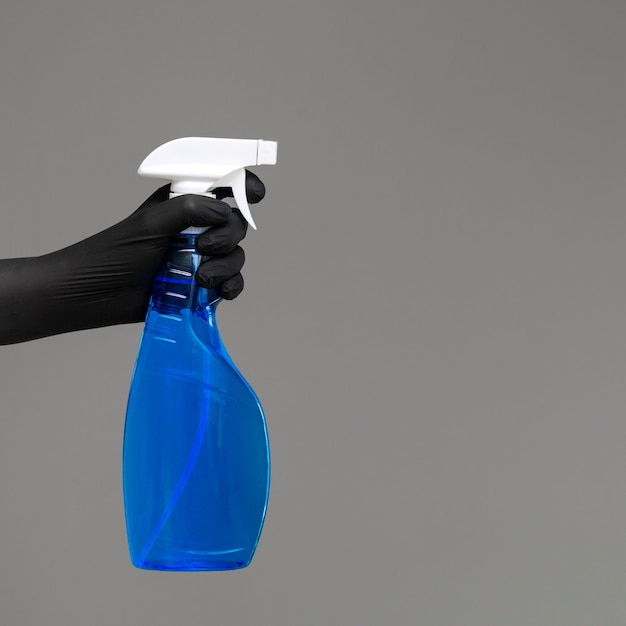 A hand in a rubber glove holds the glass cleaner in a spray bottle 