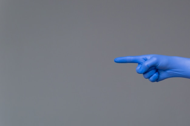 Hand in rubber glove points to the left with index finger. Neutral background , copy space.