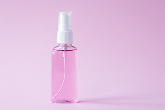 Hand sanitizer bottle, antiseptic spray for disinfection. Flacon on a pink background. Cleanser product. Antibacterial transparent gel. Copy space for text.