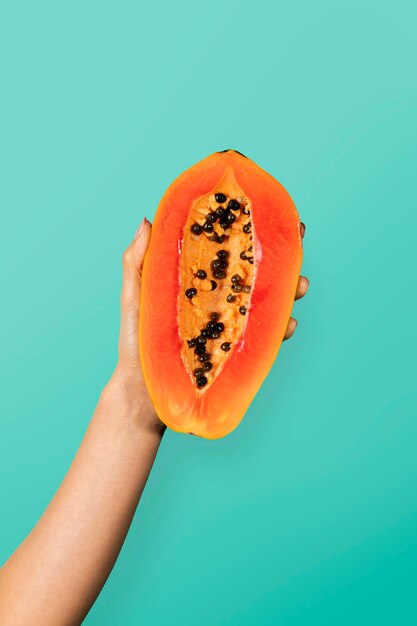 Photo hand showing a half of ripe papaya with a cyan wall